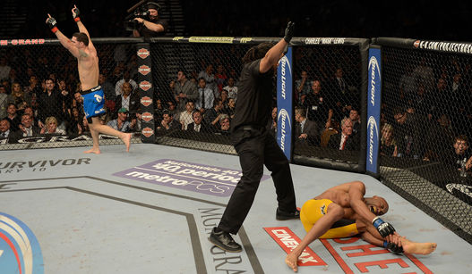 Anderson caído no chão após lesão e Weidman celebrando a manutenção do título. UFC. Foto: UFC/Divulgação