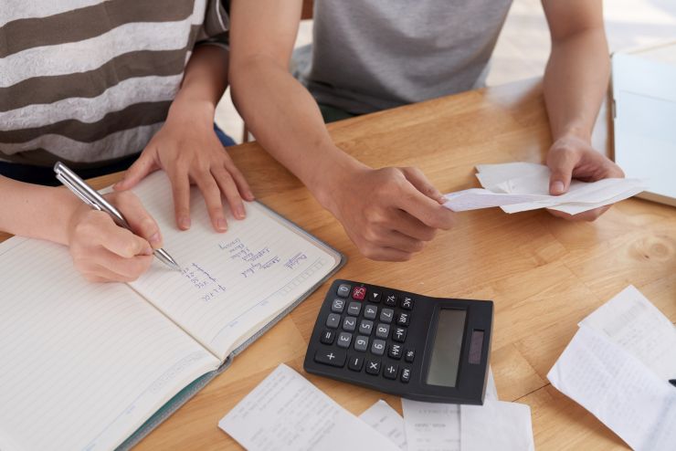 Mãos de pessoas com bloco de notas, calculadora e caneta, em posição de cálculo de dívidas