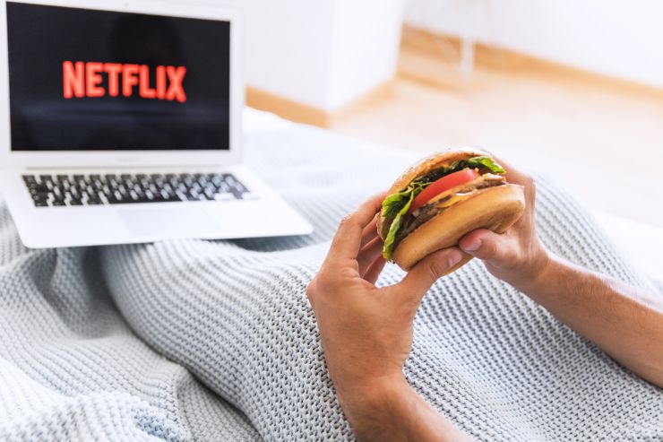 Homem segurando hambúrguer com notebook na página da Netflix