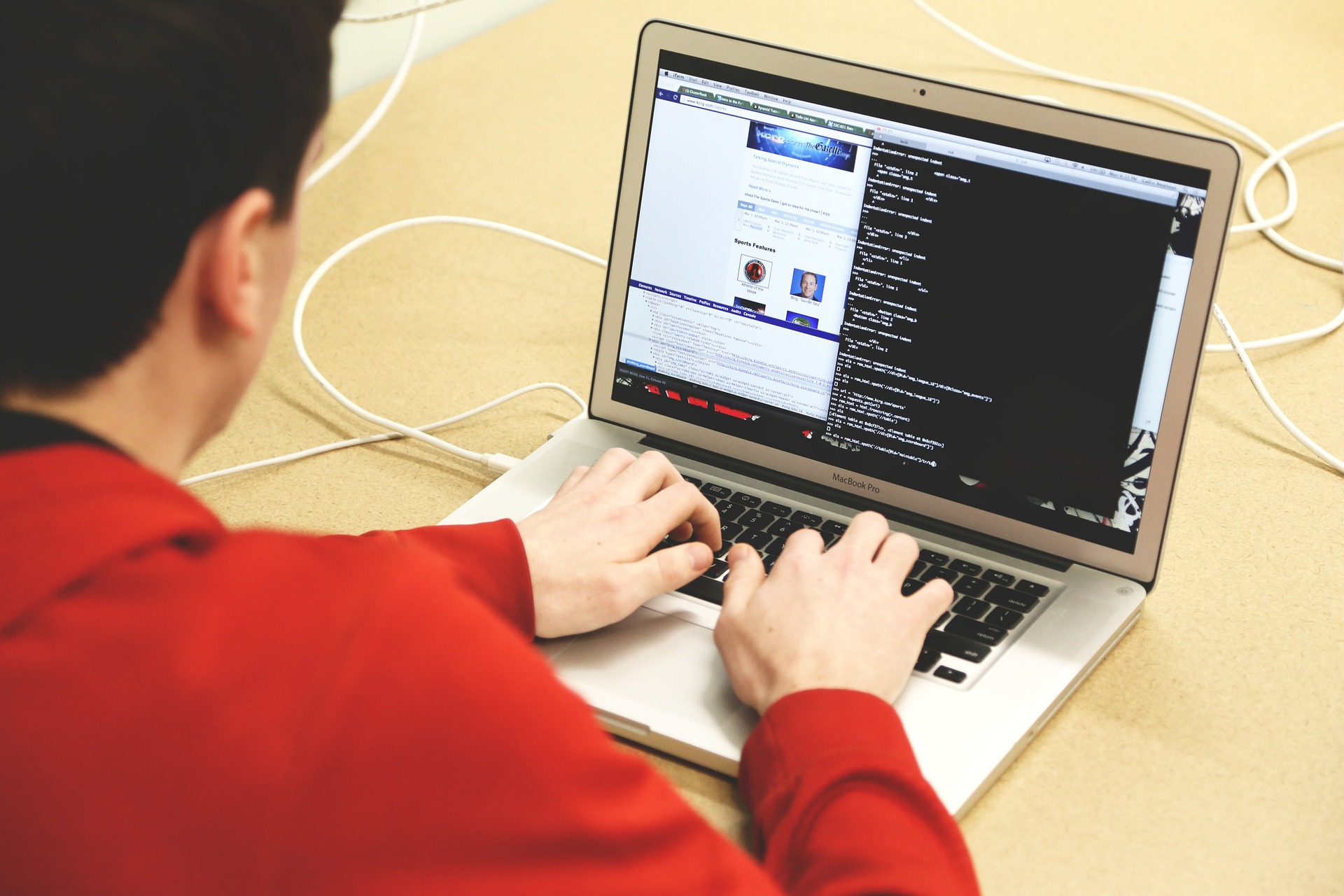 Homem de camisa laranja realiza a programação de um site em um notebook. A tela exibe diversas linhas de código.