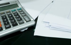 Imagem mostra uma calculadora ao lado de uma série de papéis. Ilustra a prática de investimento.