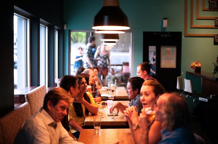 Imagem mostra várias mesas em um restaurante, como cerca de 10 pessoas conversando. Ilustra o segmento da gastronomia