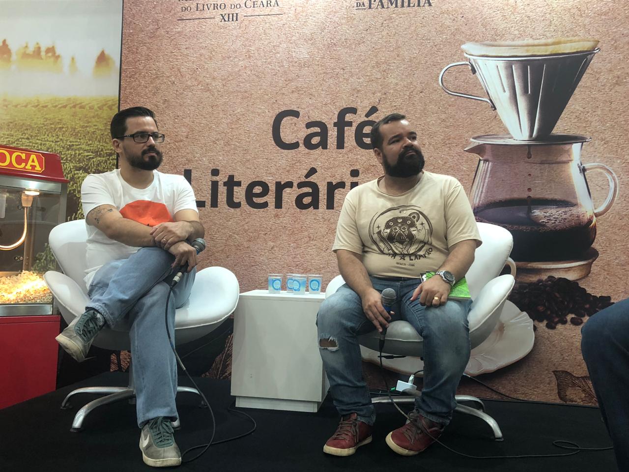 O escritor, Márcio Benjamin, de camisa branca e calça jeans, senta ao lado do autor Zé Wellington, de camisa bege e calça jeans