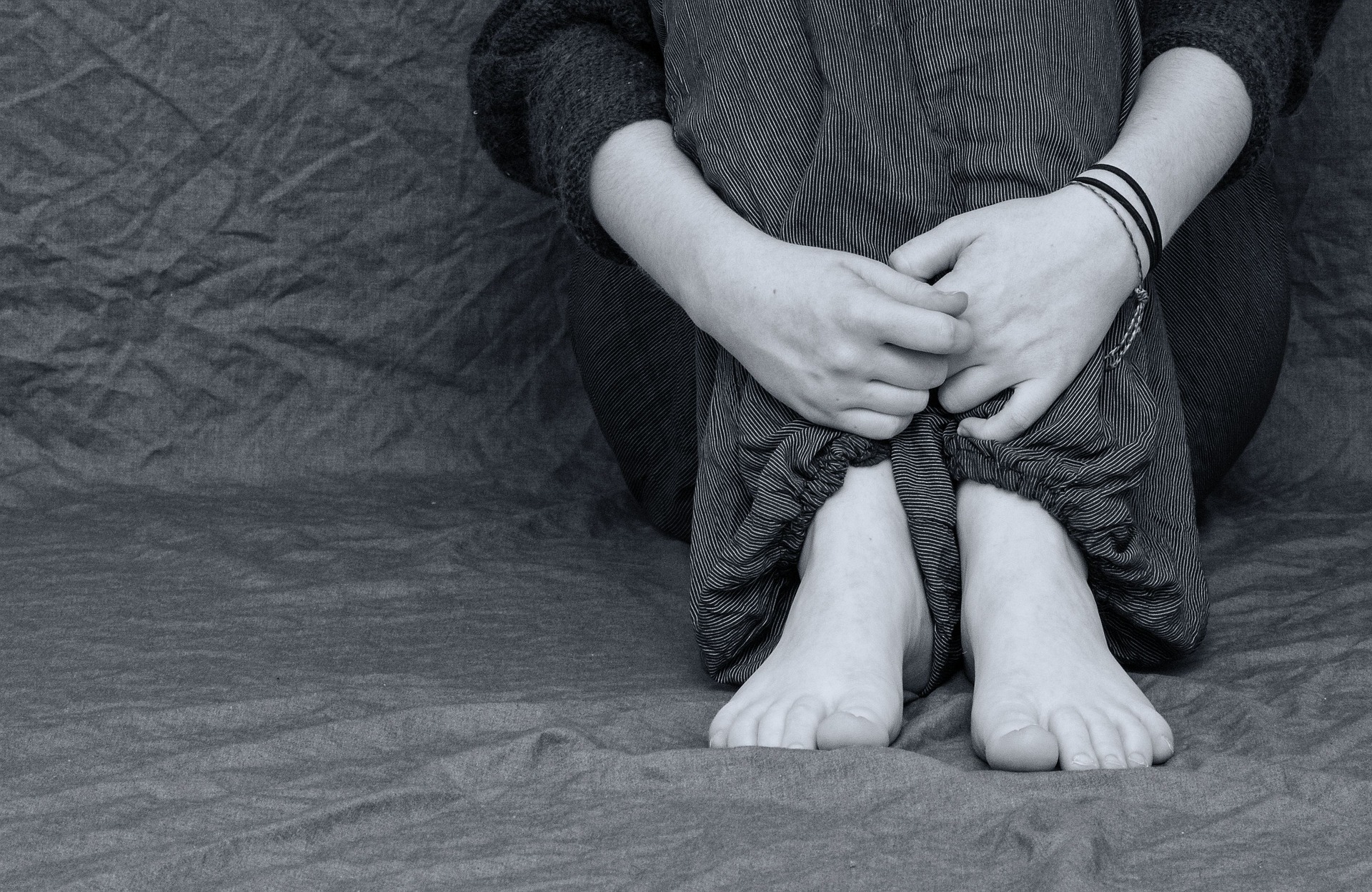 Imagem em preto e branco mostra uma pessoa sentada. O foco é em seus pés e mãos.