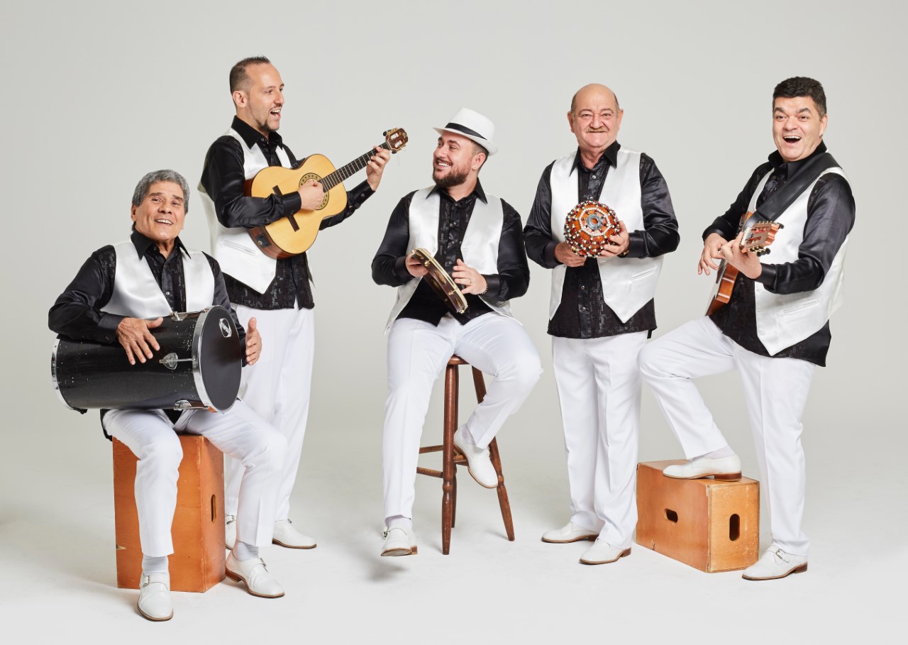 Foto do grupo Demônios da Garoa. Cinco homens em pé, com instrumentos musicais. Eles vestem roupas em preto e branco
