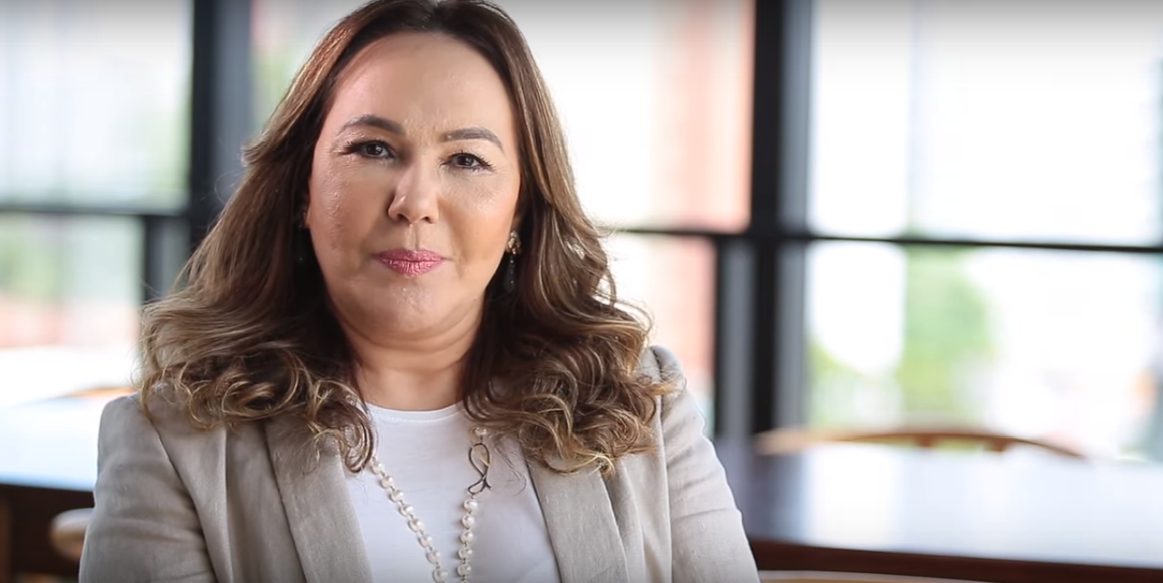 Fátima Brilhante. Mulher branca, com cabelo castanho claro. Usa um blazer cinza, com uma camisa branca por dentro e um colar.