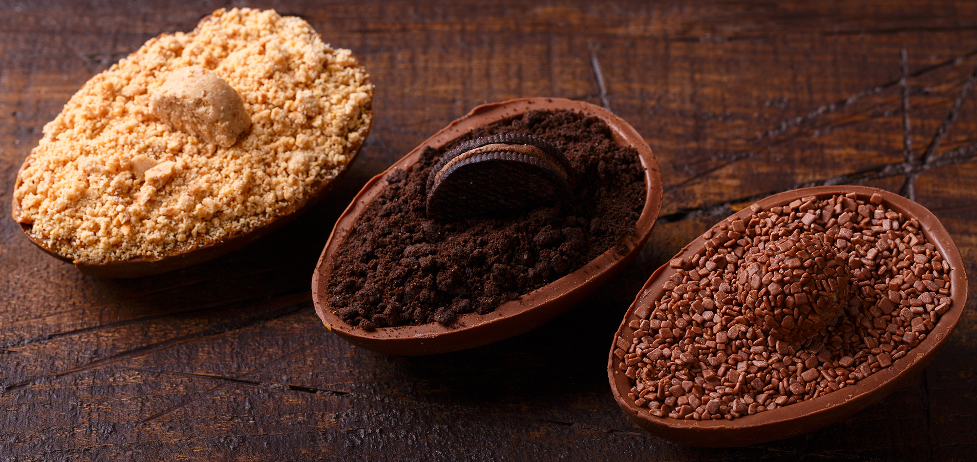 Três ovos de páscoa. Todos recheados. Um com recheio de chocolate mais claro, outro mais escuro e o terceiro com raspas de biscoito branco