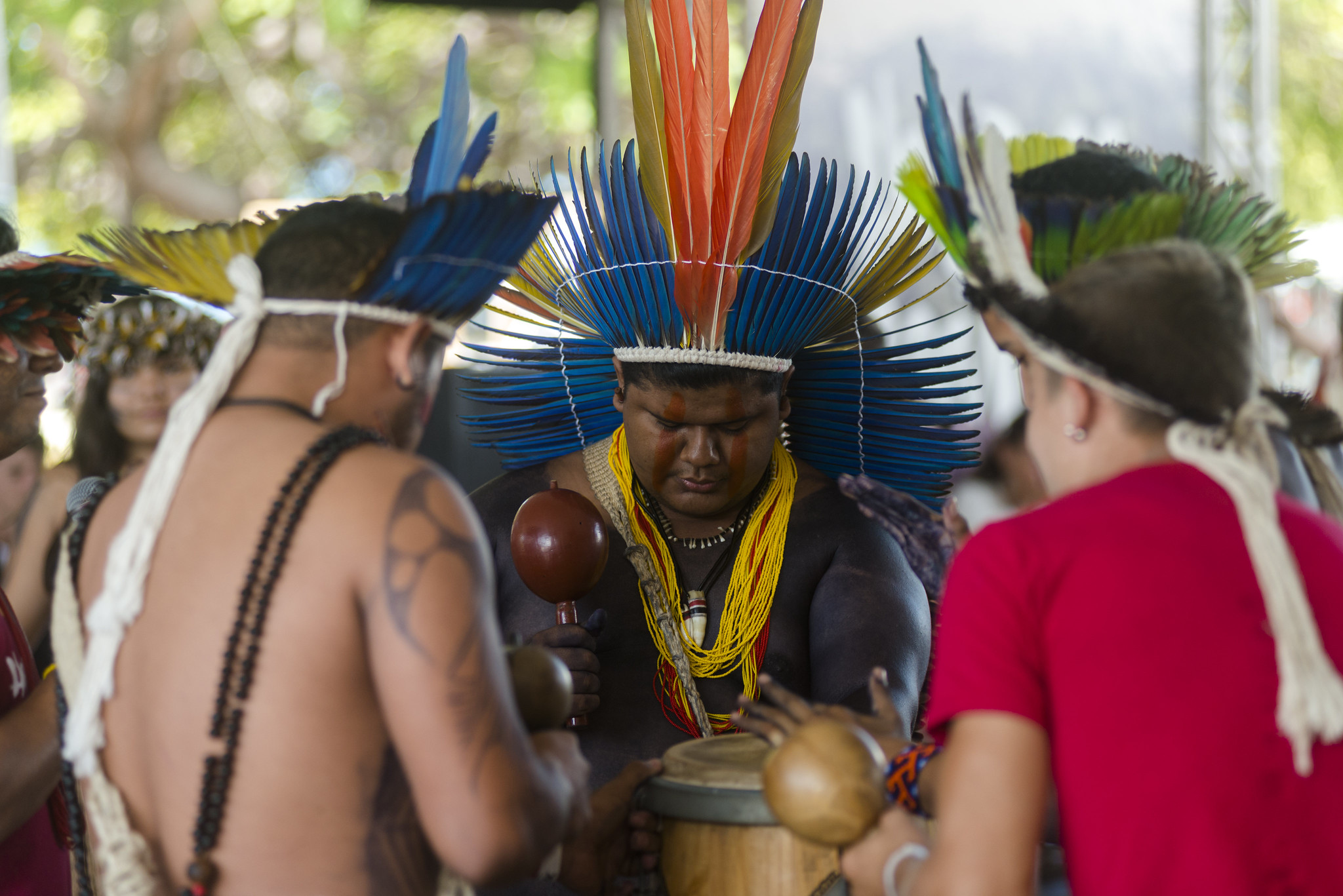 Povos tradicionais do Ceará: na imagem, três homens índigenas utilizam cocares coloridos e batem tambor juntos, em uma roda.