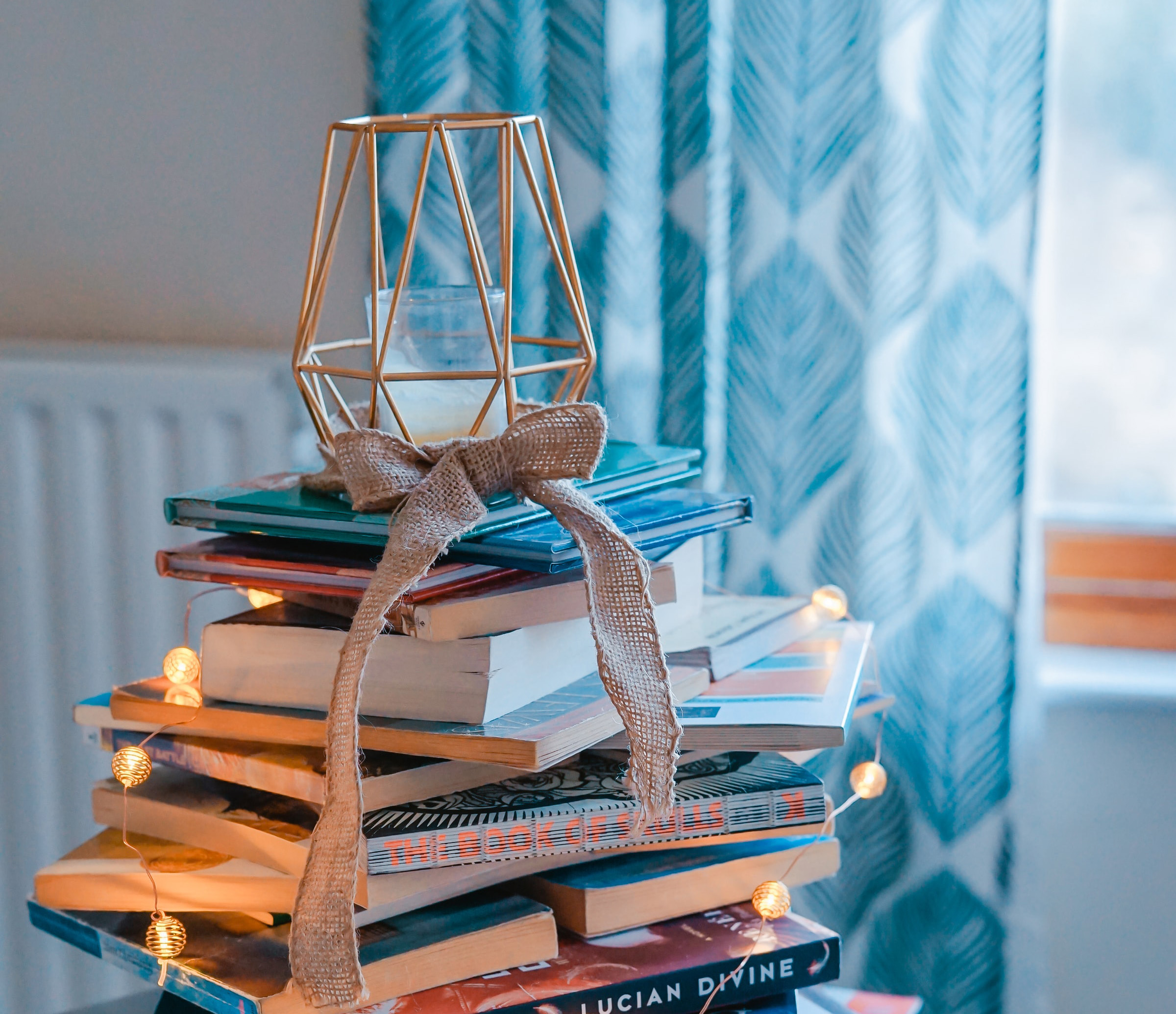 Bazar de Natal: Na imagem, vários livros estão empilhados com luzinhas de Natal ao redor, formando uma espécie de árvore improvisada.
