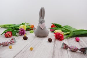 Páscoa: na imagem, um coelhinho cinza de feltro está em meio a flores e bombons coloridos.
