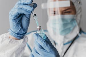 Vacinação: na imagem, um profissional da saúde devidamente paramentado manipula um frasco de imunizante com uma seringa. Ele usa máscara, luvas e faceshield.