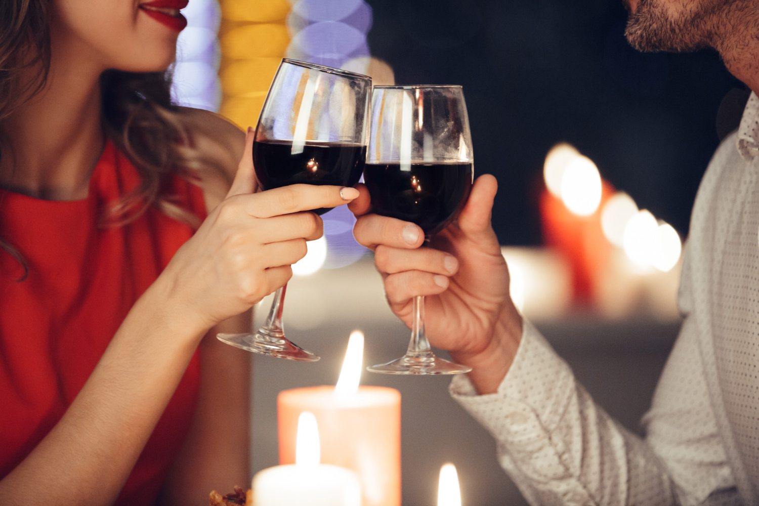 Jantar romântico: na imagem, uma mulher e um homem brindam com taças de vinho em frente a velas acesas.