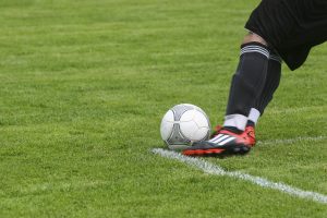 perna de um jogador de futebol chutando uma bola em campo