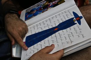 Cariri: um par de mãos folheia um caderno onde está um croqui de moda com um vestido azul