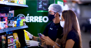 Empreendedorismo: uma mulher e um homem, ambos de máscaras, olham uma prateleira com vários alimentos. Ele usa touca e luvas descartáveis. Ao fundo, se lê "Térreo" na parede verde.