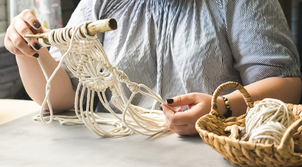 Moda sustentável: um par de mãos brancas segura um objeto artesanal feito com fios de cor clara.