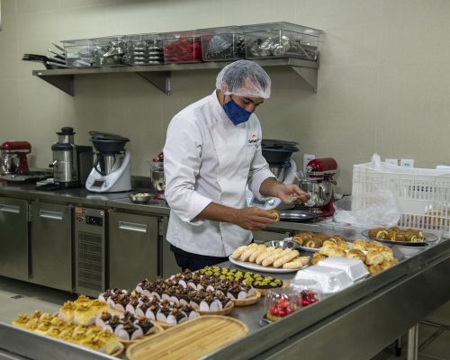 Escola de Gastronomia e Hotelaria do Ceará: a imagem mostra um homem paramentado coma dolmã, touca e máscara manipulando alimentos em frente a uma mesa.