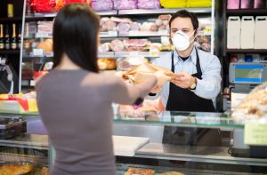 na imagem, pessoa comprando produto em supermercado, enquanto atendente utiliza uma máscara Pff2, de acordo com o novo decreto estadual