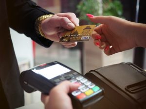 Endividamento: foto mostra uma mão entregando um cartão de crédito a outra. Há uma maquineta do cartão abaixo das mãos.
