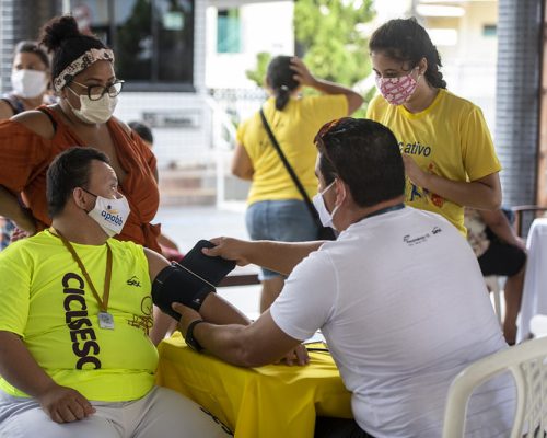 Sesc Ceará: A imagem mostra um homem tirando a pressão de outro homem. Ao lado, há duas mulheres aguardando. Todos usam máscaras de proteção e roupas casuais.