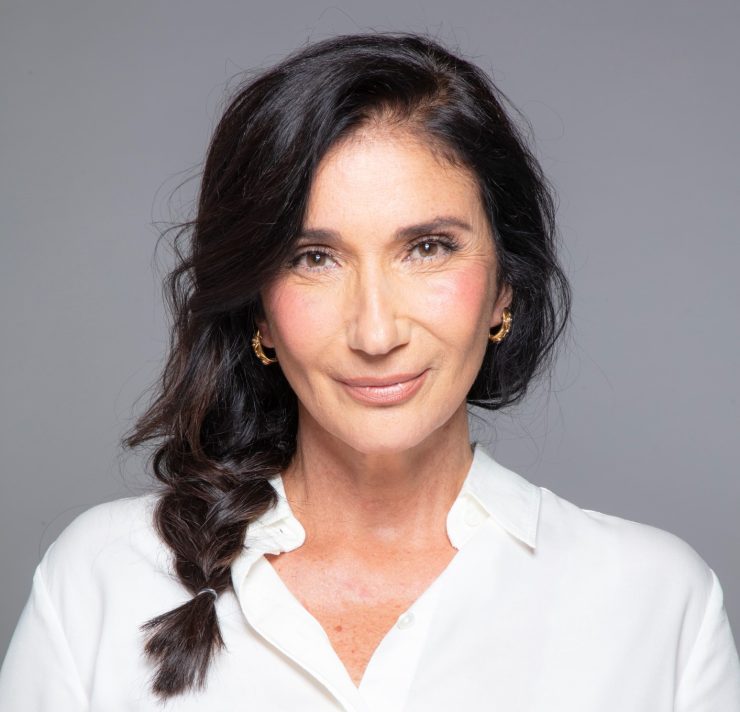 Zizi Possi: na imagem, a cantora olha para a câmera com um leve sorriso. Ela é branca, tem olhos claros, cabelo escuro e liso em uma trança e usa uma camisa social branca.