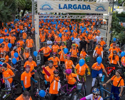 CicloSesc: imagem de uma faixa de largada com vários ciclistas com camisas laranjas e capacetes embaixo