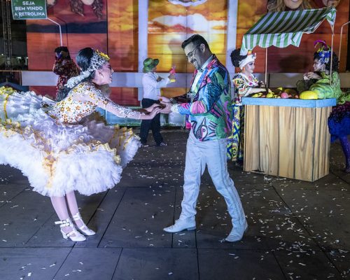 Circuito Sesc Junino: a foto mostra um casal vestido com trajes juninos enquanto dança. A mulher usa vestido bufante amarelo e o homem, uma calça branca com camisa estampada.