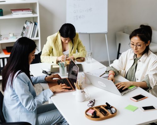 Qualificação profissional: três mulheres digitam em notebooks e escrevem em uma mesa