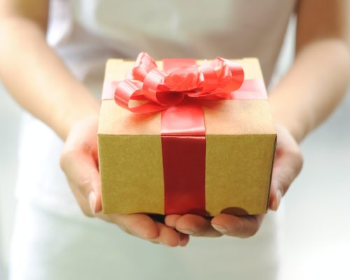 Dia das Mães: foto mostra um par de mãos brancas segurando uma caixa de presente amarela com laço vermelho