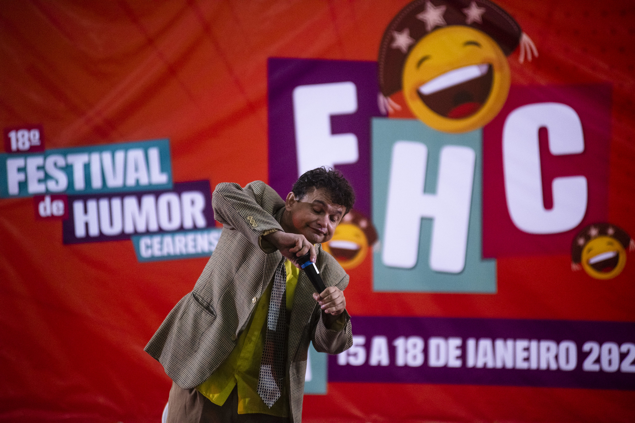 Festival de Humor Cearense: Um homem de terno se apresenta em frente a um banner onde se lê "Festival do Humor Cearense"