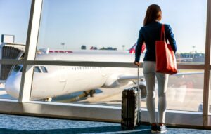Turismo em Fortaleza: a imagem mostra uma mulher em pé, segurando uma mala, em frente a um avião